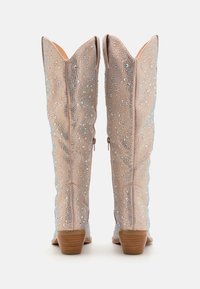 Korálkové kovbojské boty v světle béžové barvě s špičatou špičkou, rozšířenými vršky a jemnými třpytivými detaily, s krátkým dřevěným podpatkem a bočními zipy.
