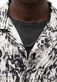 Camicia a maniche corte con un motivo astratto in bianco e nero, dotata di colletto con bottoni e di una t-shirt nera a strati sotto, realizzata in tessuto testurizzato.