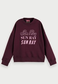 Sudadera morada oscura con "Sun Ray" impreso tres veces en diferentes fuentes rosas en la parte frontal, con mangas largas y puños de canalé.
