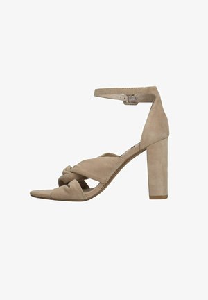 Sandale à talon haut en suède beige avec un épais talon bloc rectangulaire, un design de bride nouée sur le devant du pied, et une bride de cheville.