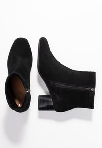 Bottines en daim noir avec bout arrondi, fermeture éclair latérale et talon bloc texturé. Doublure intérieure lisse.