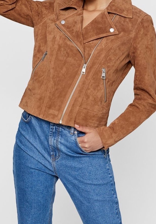 Veste cropped en daim marron avec un col incrusté, des fermetures éclair argentées et deux poches avant. Portée avec un jean en denim bleu.