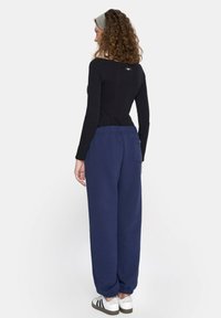 Czarna bluzka z długim rękawem i niebieskie dresy z elastycznymi mankietami. Ubranie ma prosty design i jest zestawione z białymi trampkami.