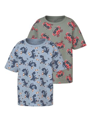 Dos camisetas de manga corta para niños, una verde con cangrejos rojos que llevan gafas de sol y otra azul con dinosaurios azul oscuro montando monopatines.