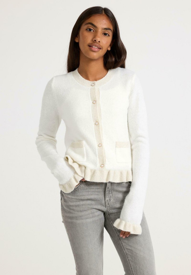 White cardigan with a round neckline, front pockets, and ruffled cuffs. Features beige accents and buttons, made from fluffy material.