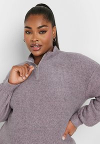 Helllila Fleece-Pullover mit halbem Reißverschluss-Kragen, strukturiertem Stoff, überschnittenen Schultern und langen Ärmeln. Bemerkenswerte Nahtdetails und weicher Fall.