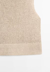 Beige gestrickte ärmellose Pulloverweste mit geripptem Saum vor weißem Hintergrund, zeigt Textur und Stichdetails.