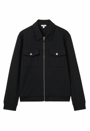 Chaqueta negra con cremallera fabricada con un tejido de textura suave. Presenta un cuello, dos bolsillos frontales con cierres de botón y puños de canalé.