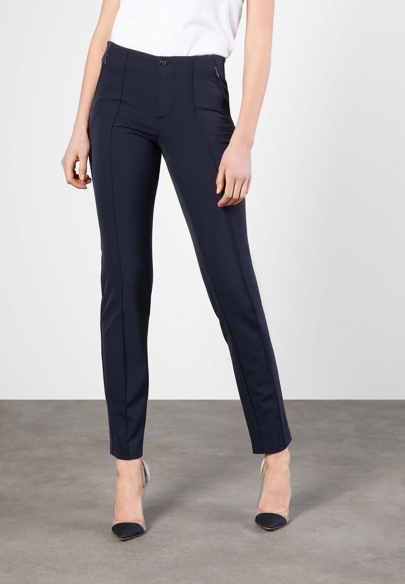 Navy slim-fit bukser laget av elastisk stoff. Har en glidelåslomme og fremre sømmer. Brukt med transparente stilettos.