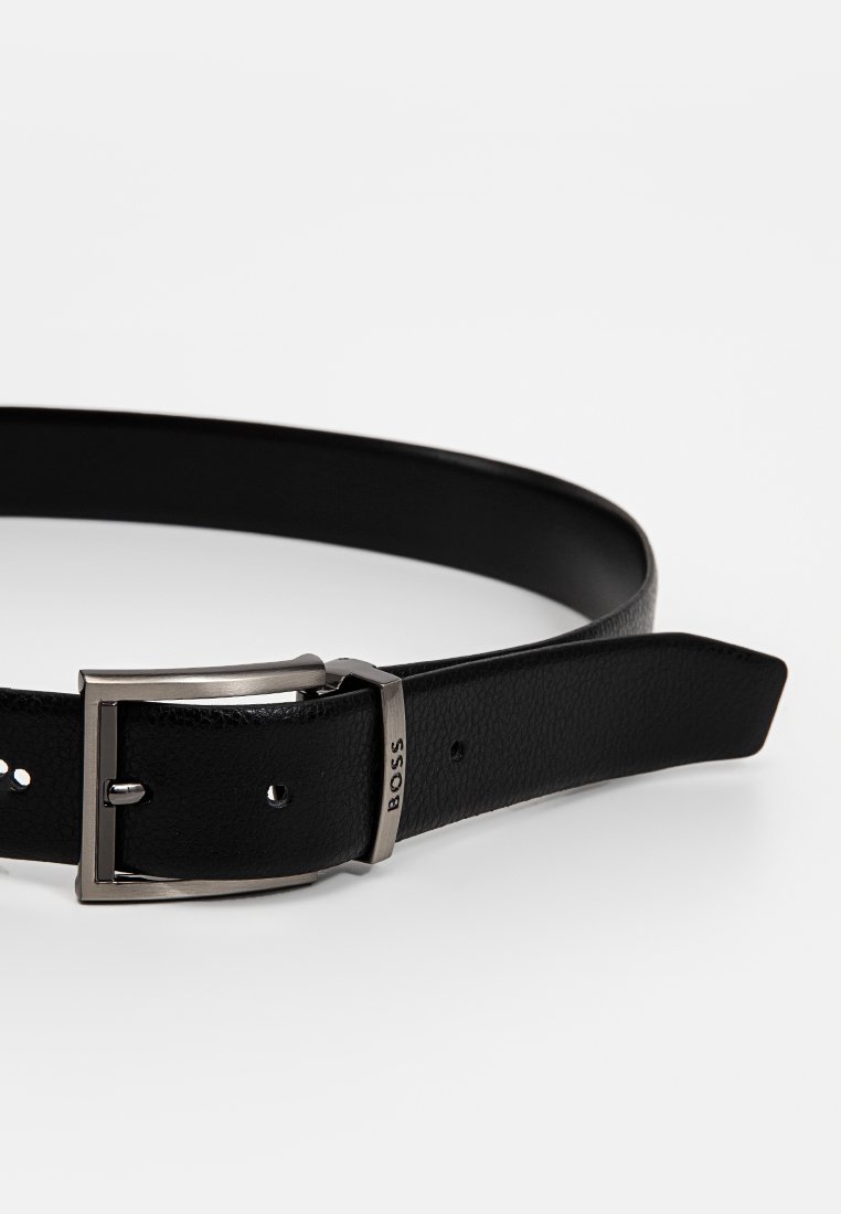 Cintura in pelle nera con una texture liscia, fibbia in metallo argentato e logo del brand sul lato della fibbia. Design classico e slim.