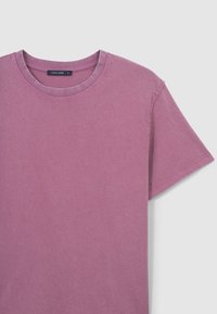 T-shirt a maniche corte in cotone rosa sbiadito. Presenta un colletto rotondo e orli cuciti, con una vestibilità rilassata e una texture morbida.