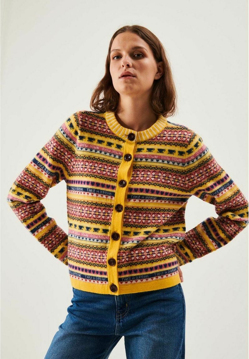 Stickad cardigan med en gul botten och flerfärgade geometriska mönster, rund krage och mörka knappar framtill.