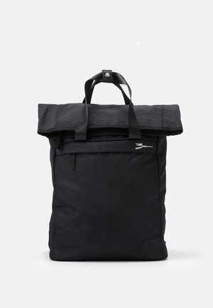 Sac à dos noir à enroulement avec poche zippée à l'avant et double poignées, tissu texturé, et petit logo blanc sur le haut avant.