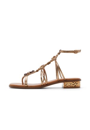 Sandale métallique dorée avec bride à la cheville, éléments floraux décoratifs, bout ouvert et petit talon bloc avec un accent à motif.