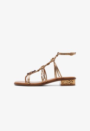 Sandale métallique dorée avec bride à la cheville, éléments floraux décoratifs, bout ouvert et petit talon bloc avec un accent à motif.