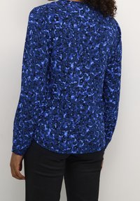 Blusa a maniche lunghe blu con motivo a fiori che presenta una combinazione di tonalità di blu scuro e chiaro, texture liscia, orlo arrotondato e vestibilità morbida.