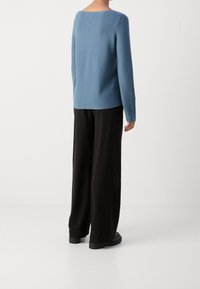 Maglione blu con scollo quadrato e maniche lunghe, abbinato a pantaloni neri larghi e stivaletti neri robusti. Tessuto liscio.