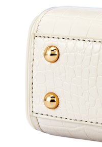 Róg białej torebki z teksturowanej skóry z złotymi nitami i kontrastującymi szwami. Skupienie na detalach dotykowych i eleganckim designie.