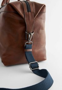 Brun läderväska med en strukturerad yta, med ett marinblått band och silverdetaljer. Innehåller dragkedjestängning och vikbar design.