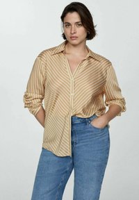 Camicia a righe, giallo chiaro, con bottoni e maniche lunghe, vestibilità comoda e un sottile lucido, abbinata a jeans blu a vita alta.