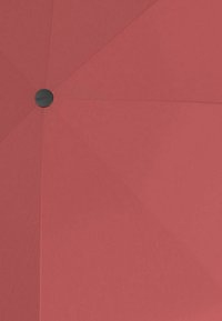 Paraguas rojo con forma plana, hecho de material textil, que presenta un botón negro central. La superficie tiene una textura suave sin patrones.