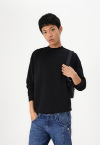 Black pullover with a round neckline and long sleeves, paired with blue denim jeans featuring side pockets and stitching details.