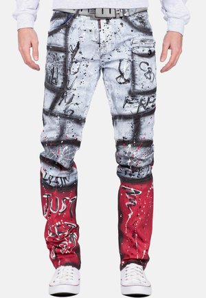 Jeans avec un dégradé bleu clair délavé et rouge, des éclaboussures de peinture et du texte graffiti. Comprend des poches et une ceinture noire avec des accents métalliques.