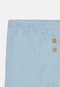 Lichtblauwe katoenen shorts met elastische tailleband, voorzien van twee houten knopen en contrasterende stiksels langs de zijnnaad.