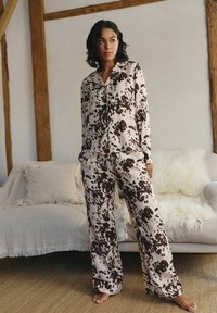 Svetle barevné pyžamo s potiskem kravské kůže v tmavě hnědé barvě. Vrchní část má límec a knoflíky; široké kalhoty dotvářejí outfit.