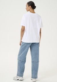 White cotton t-shirt with a relaxed fit, paired with loose light blue denim pants. The outfit features a simple design and clean lines.