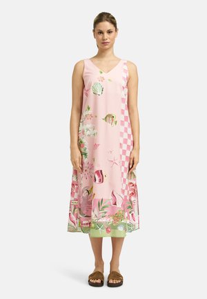 Woman wearing a sleeveless pink dress with sea-themed prints and a green hem, standing straight on a plain light background.