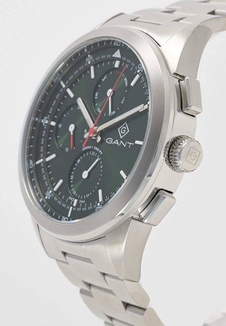 Reloj cronógrafo de acero inoxidable con una esfera verde oscura, tres subesferas, marcadores de hora plateados y acentos rojos. Resistente al agua hasta 100 metros.