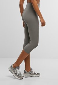 Grå capri leggings med høy midje, glatt tekstur, tettsittende design, kombinert med grå treningsko med mesh og snøre detaljer.