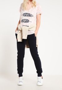 Ljusrosa V-ringad t-shirt med fjädergrafik; ihop med mörkblå joggingbyxor och vita sneakers. Stickad tröja knuten i midjan.