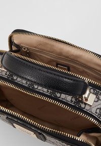 Sort struktureret håndtaske med en tekstureret overflade, guld lynlåse og en beige indvendig. Har et logomærke og en indvendig lynlås lomme.