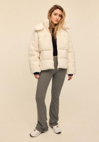 Hvid, blød dunjakke med store quiltede sektioner og høj krave, kombineret med sorte og hvide stribede vidde bukser og hvide sneakers.