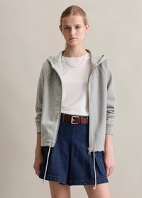 Grau zipfel Hoodie mit Kordelzügen, getragen über einem weißen Shirt, kombiniert mit einem Dunkelblauen Jeansrock und einem braunen Gürtel mit einer silbernen Schnalle.