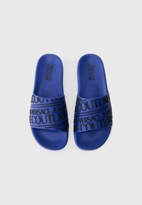 Blue slide sandals featuring a textured sole and a bold black design with "VERSACE JEANS COUTURE" across the strap.