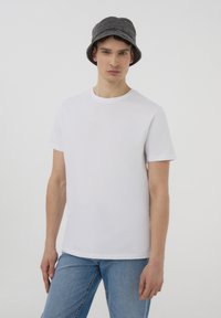 Biała bawełniana koszulka z okrągłym dekoltem, krótkimi rękawami i prostym dołem, w połączeniu z jasnoniebieskimi dżinsami i szarym kapeluszem typu bucket.