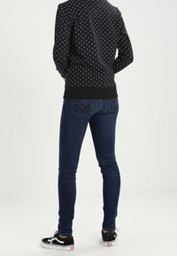 Svart sweatshirt med prickar, mörkblå skinny jeans och svarta sneakers. Sweatshirten har en ribbad nederkant och ribbade ärmslut. Jeansen har bakfickor.