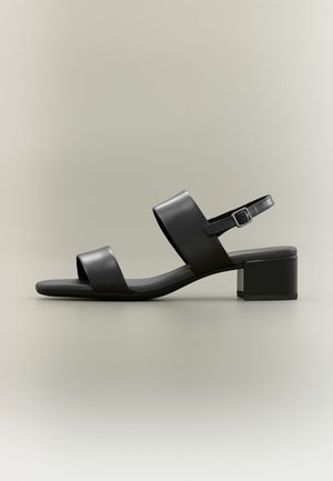 Black leather open-toe sandal with two wide straps, ankle buckle, and low block heel on a neutral background.