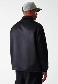 Black satin jacket with a smooth texture, relaxed fit, and elastic cuffs. Features a stand-up collar and a clean, minimalistic design.