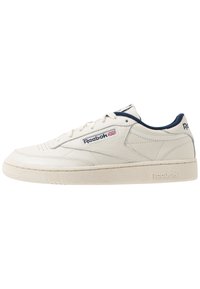 Zapatilla de cuero blanca con acentos en azul marino, diseño de cordones planos, suela de goma texturizada y logo de Reebok en el lateral y en la lengua.