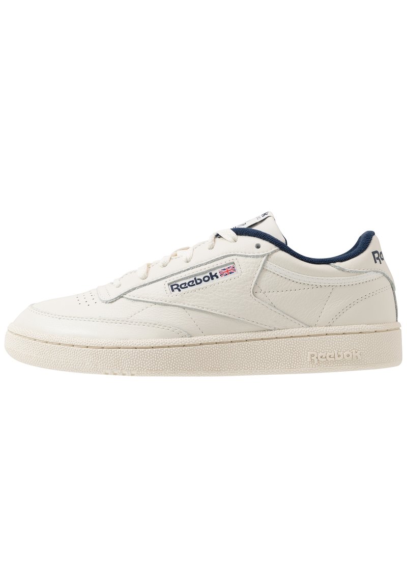 Zapatilla de cuero blanca con acentos en azul marino, diseño de cordones planos, suela de goma texturizada y logo de Reebok en el lateral y en la lengua.