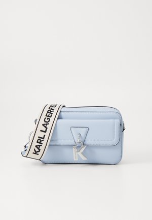 Sac rectangular bleu clair en matériau lisse, avec un charme en argent en forme de K, fermeture éclair et bandoulière rayée réglable.