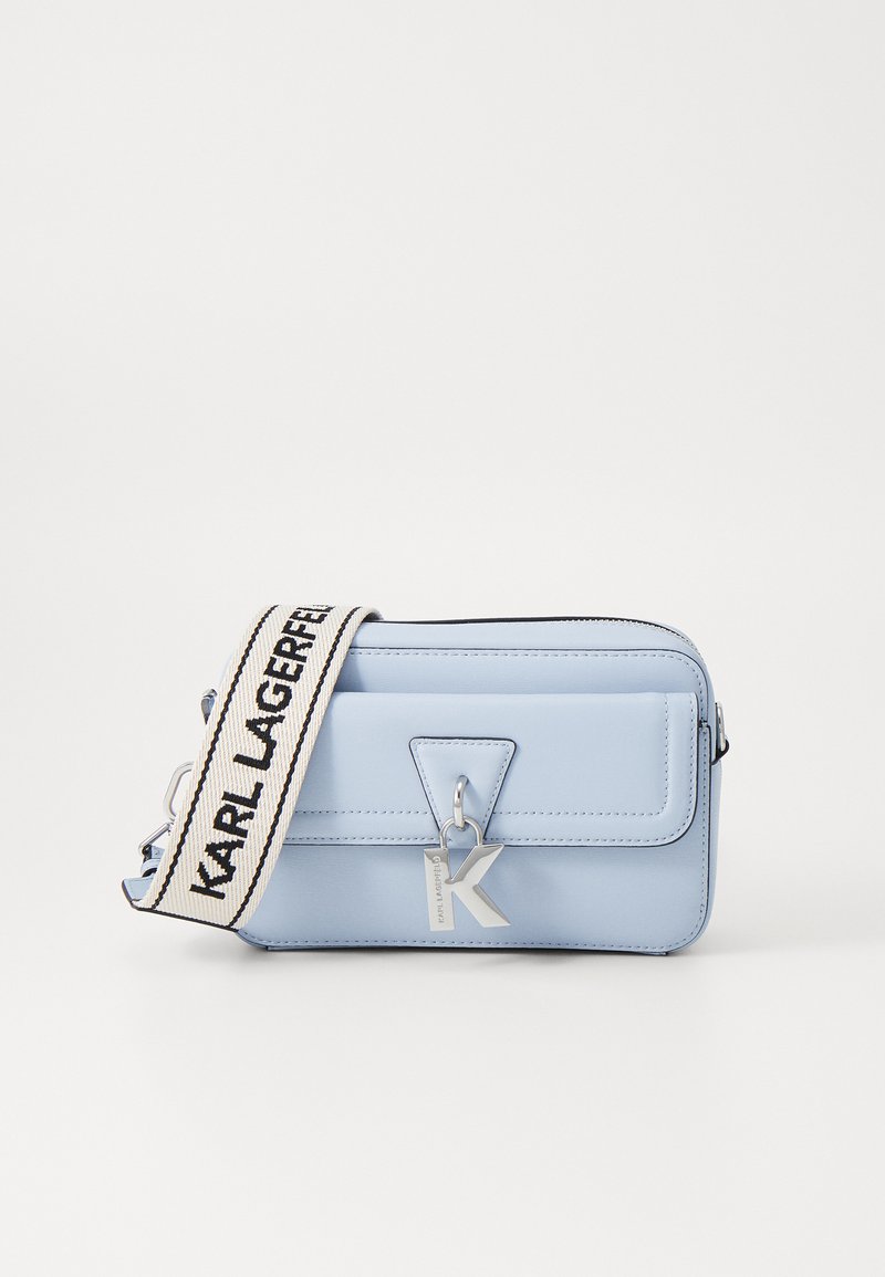 Ljusblå rektangulär crossbody-väska gjord av slätt material, med en silverfärgad K-charms, dragkedjeslutning och justerbar randig axelrem.