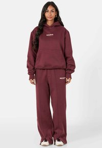 Bordeaux hoodie en bijpassende trainingsbroek van een zachte stof, met een voorzak en een geborduurd logo op de borst en dij.