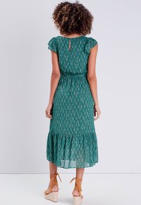 Green patterned dress with ruffled cap sleeves, a keyhole back, and a tiered hem. Paired with tan wedge sandals.