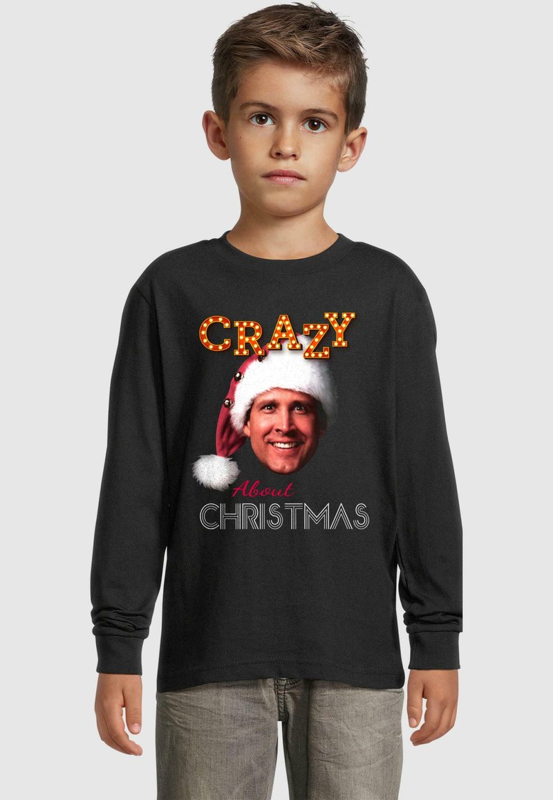 Must värvi pikkade varrukatega T-särk, millel on prinditud tekst "CRAZY" valgustatud stiilis ja "About CHRISTMAS" allpool, koos graafikaga mehest, kellel on peal Jõuluvana müts.