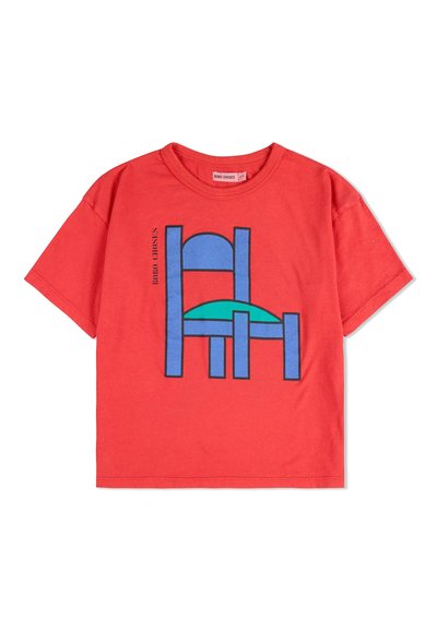 Rød bomulds t-shirt med et grafikdesign af en blå stol med en teal sæde. T-shirten har korte ærmer og rund halsudskæring.